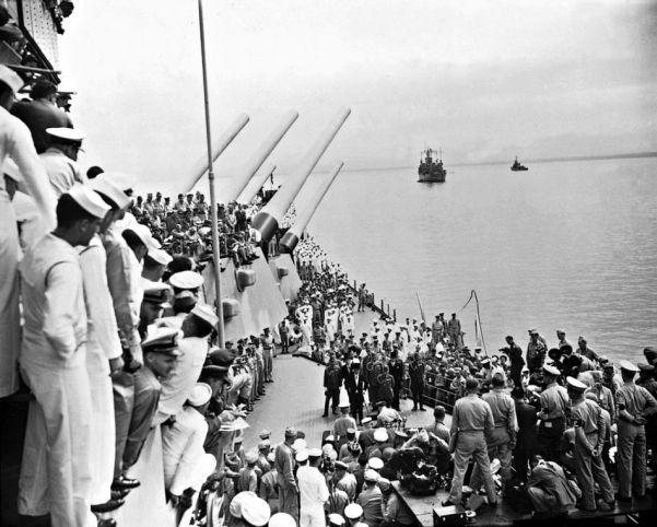 Sailors and officials on the deck of the USS Missouri witness the Japanese sign surrender documents in Tokyo Bay